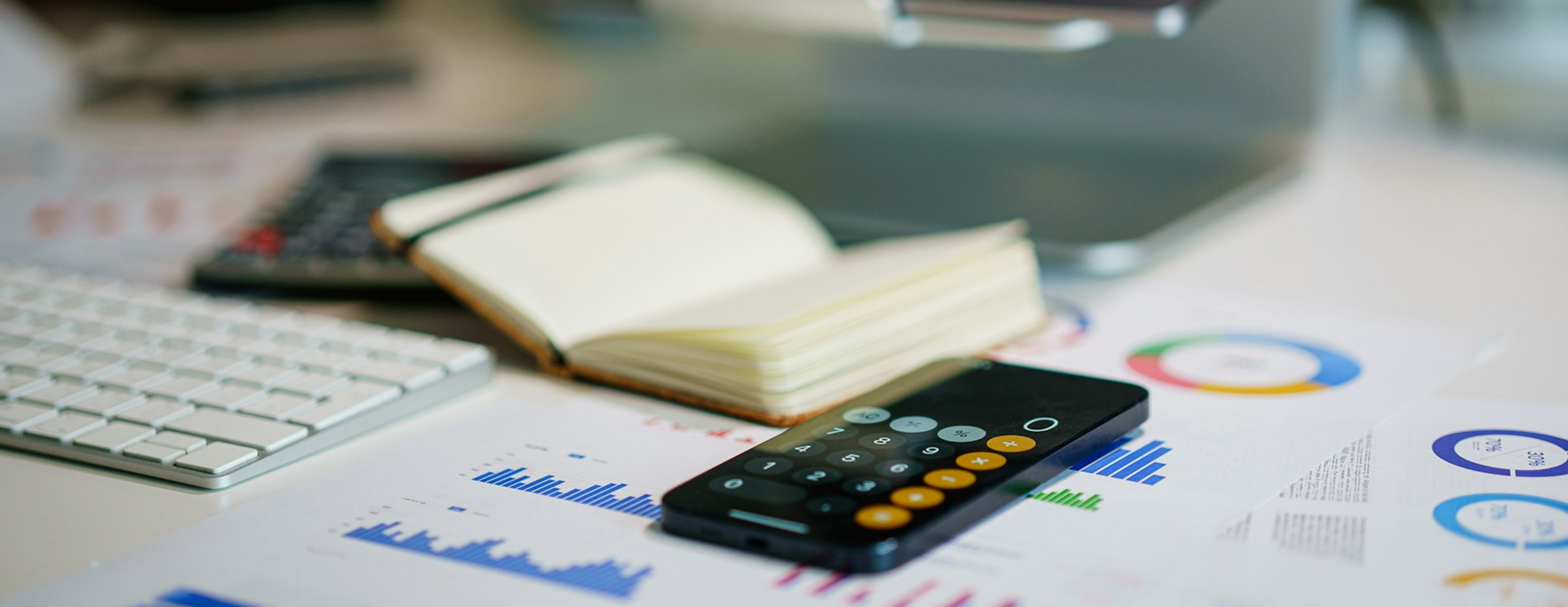 An iPhone calculator on a desk with a notebook and papers with charts